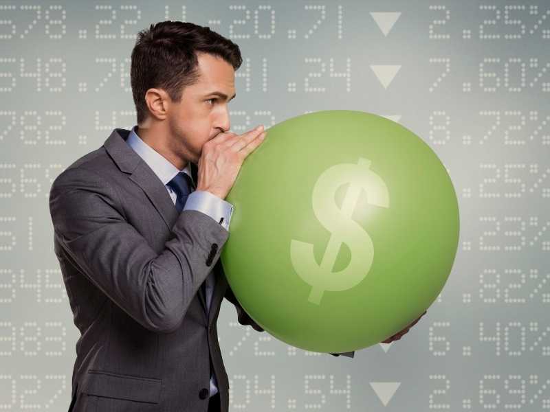 Hombre en traje inflando un globo con símbolo de dinero simulando inflación y el porqué suben los precios